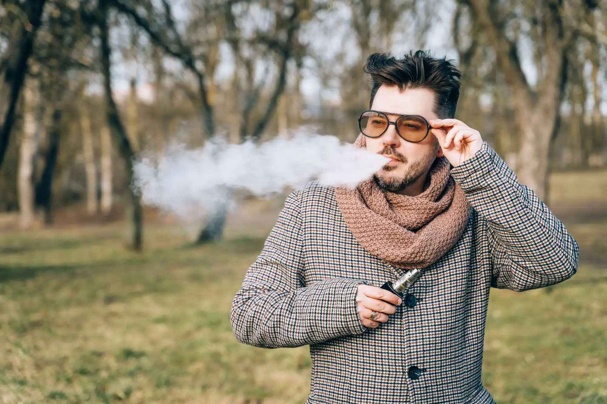 Bearded man in sunglasses vaping outdoors