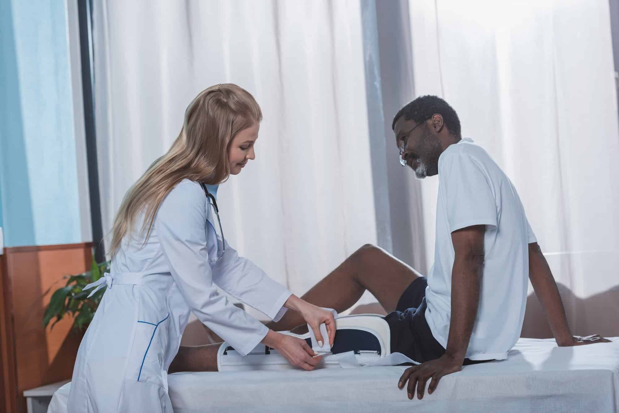 Female doctor straps leg brace on male patient