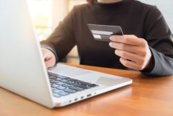 One hand holds credit card while other hand works on laptop