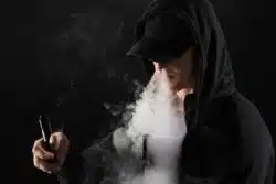Man in black cap and hoodie blows vape cloud