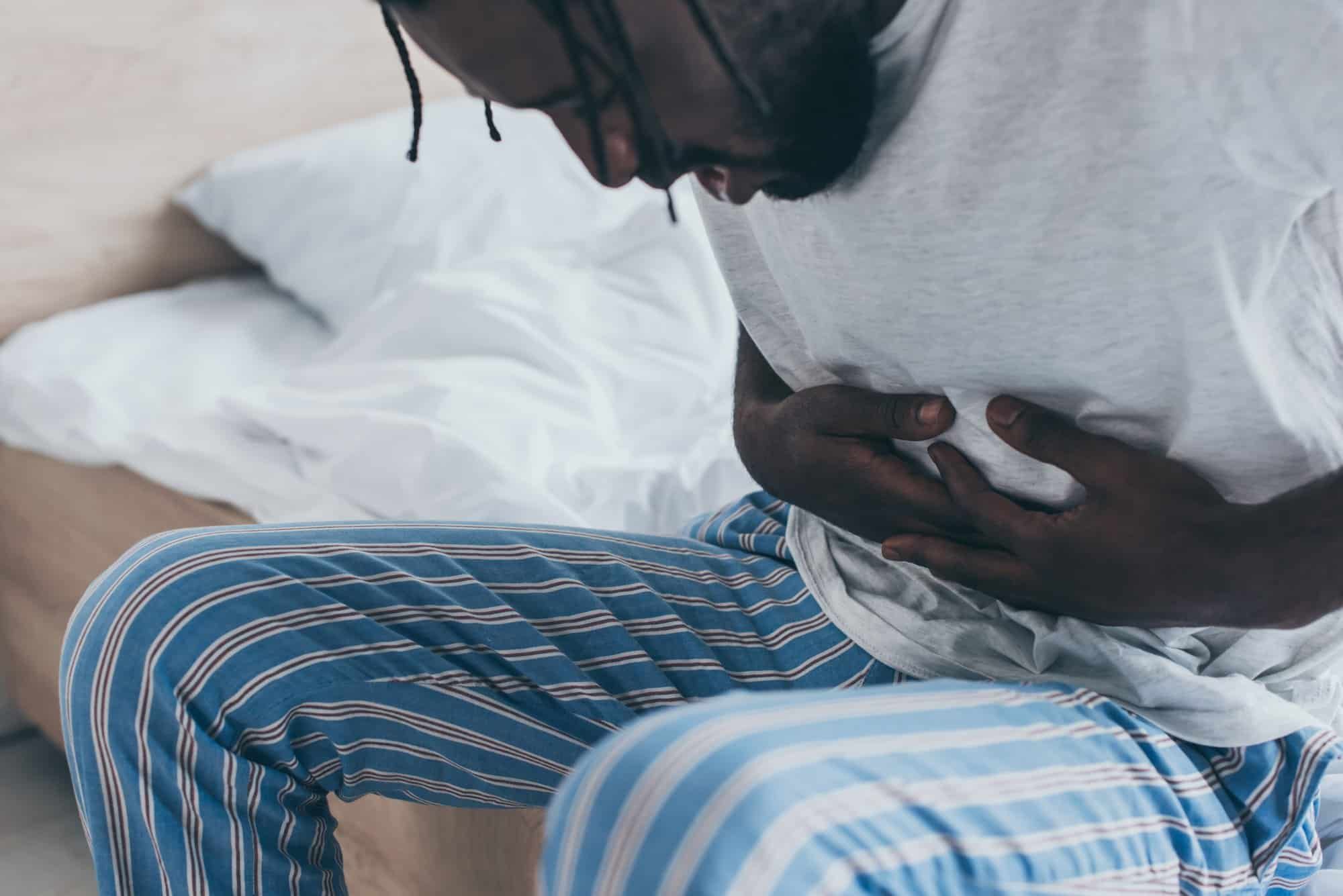 Man sits on edge of bed holding stomach in pain