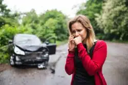 Upset woman on cell phone with wrecked car in background