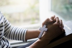 Closeup of woman holding cross necklace, hands folded over Bible