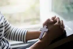 Closeup of woman holding cross necklace, hands folded over Bible