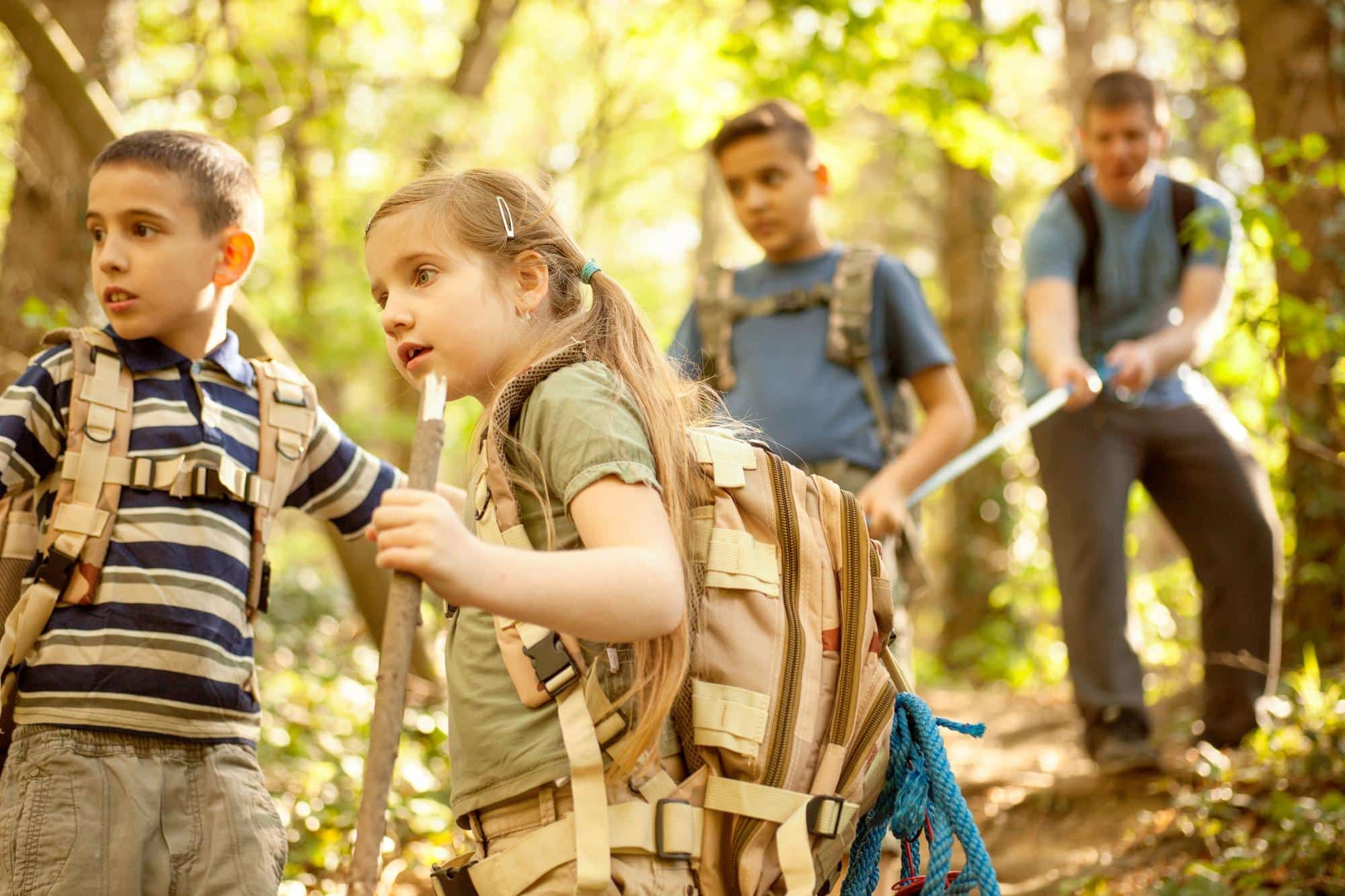 Two boys and a girl on a hike in the woods with male adult leader
