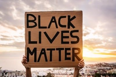 A protester holds a cardboard "Black Lives Matter" sign above their head - excessive force