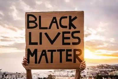 A protester holds a cardboard "Black Lives Matter" sign above their head - excessive force