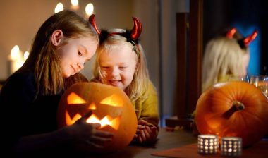 Two young girls carve light a jack-o-lantern, with candles in the background - safety tips on halloween