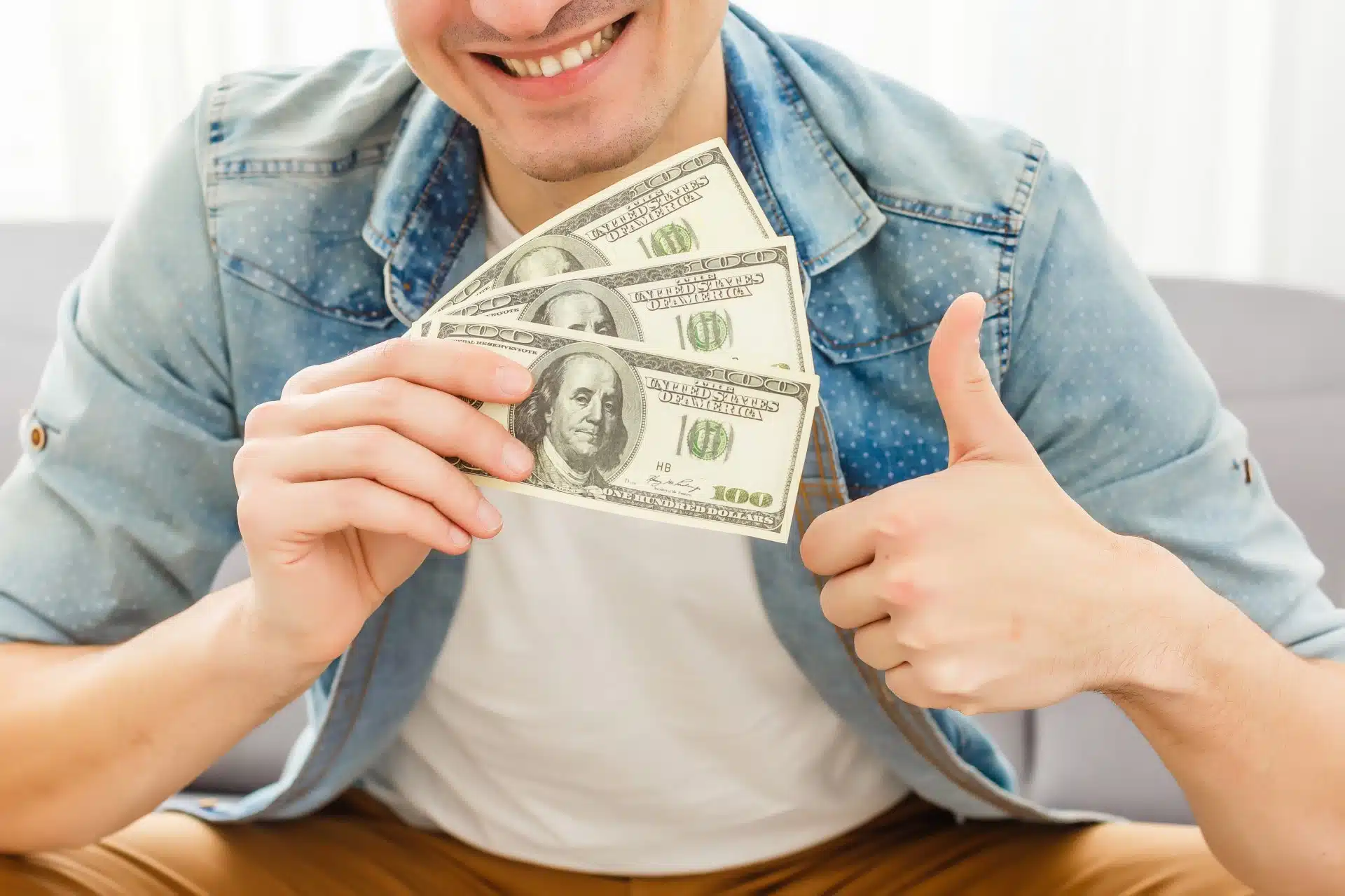 Man holds three $100 bills fanned out and gives a thumbs up - class action settlement checks