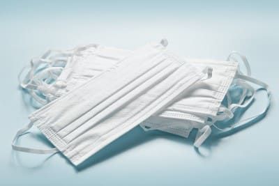 A stack of white medical face masks on a light blue background - PPE shortage