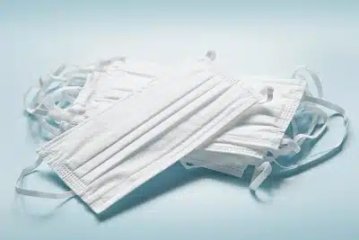 A stack of white medical face masks on a light blue background - PPE shortage
