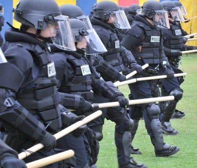 Police officers in riot gear stand in a line - police brutality