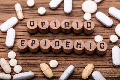Cylindrical letter blocks spell out "opioid epidemic" surrounded by pills - opioid crisis