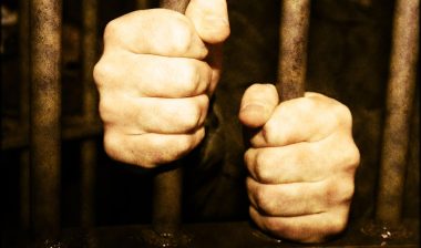 A prisoner holds two vertical bars of their cell - aclu of minnesota