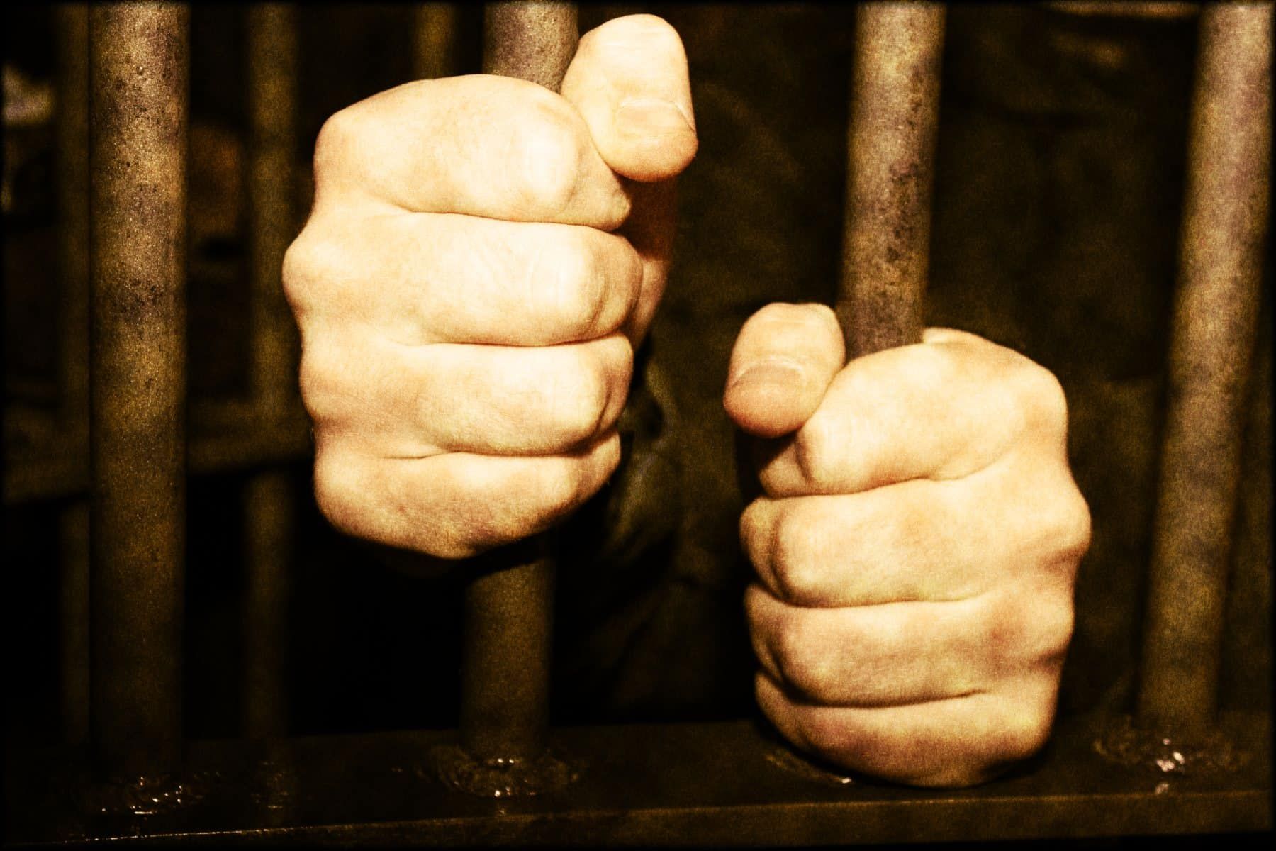 A prisoner holds two vertical bars of their cell - aclu of minnesota
