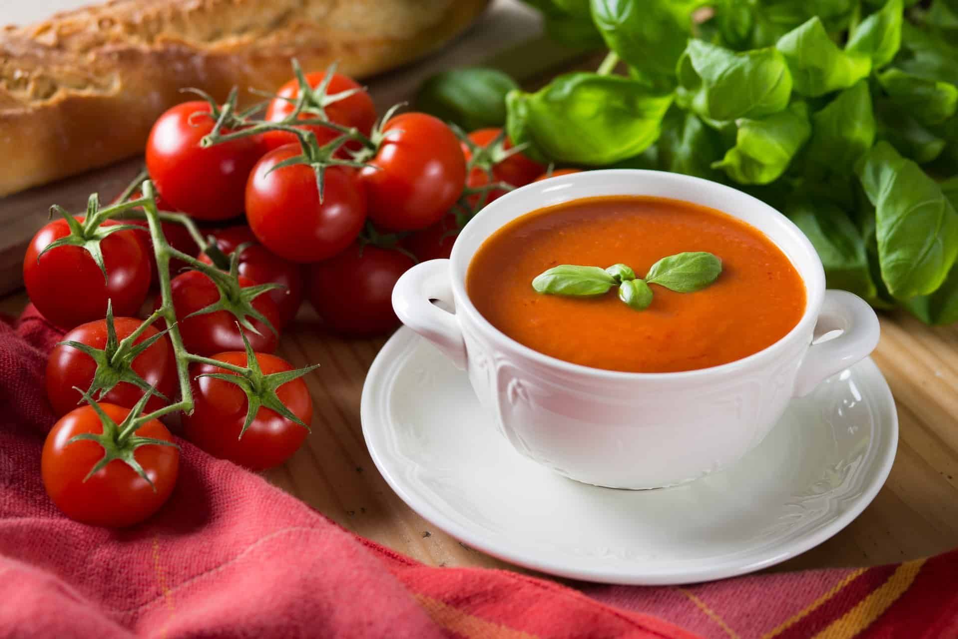 Tomato soup in a white bowl with tomatoes sitting nearby - Campbell's soup