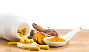 Powdered turmeric in a spoon next to whole turmeric and turmeric pills - pain relief