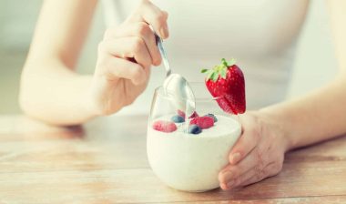 A woman's hands hold a glass of yogurt and fruit as she digs in a spoon - chobani greek yogurt
