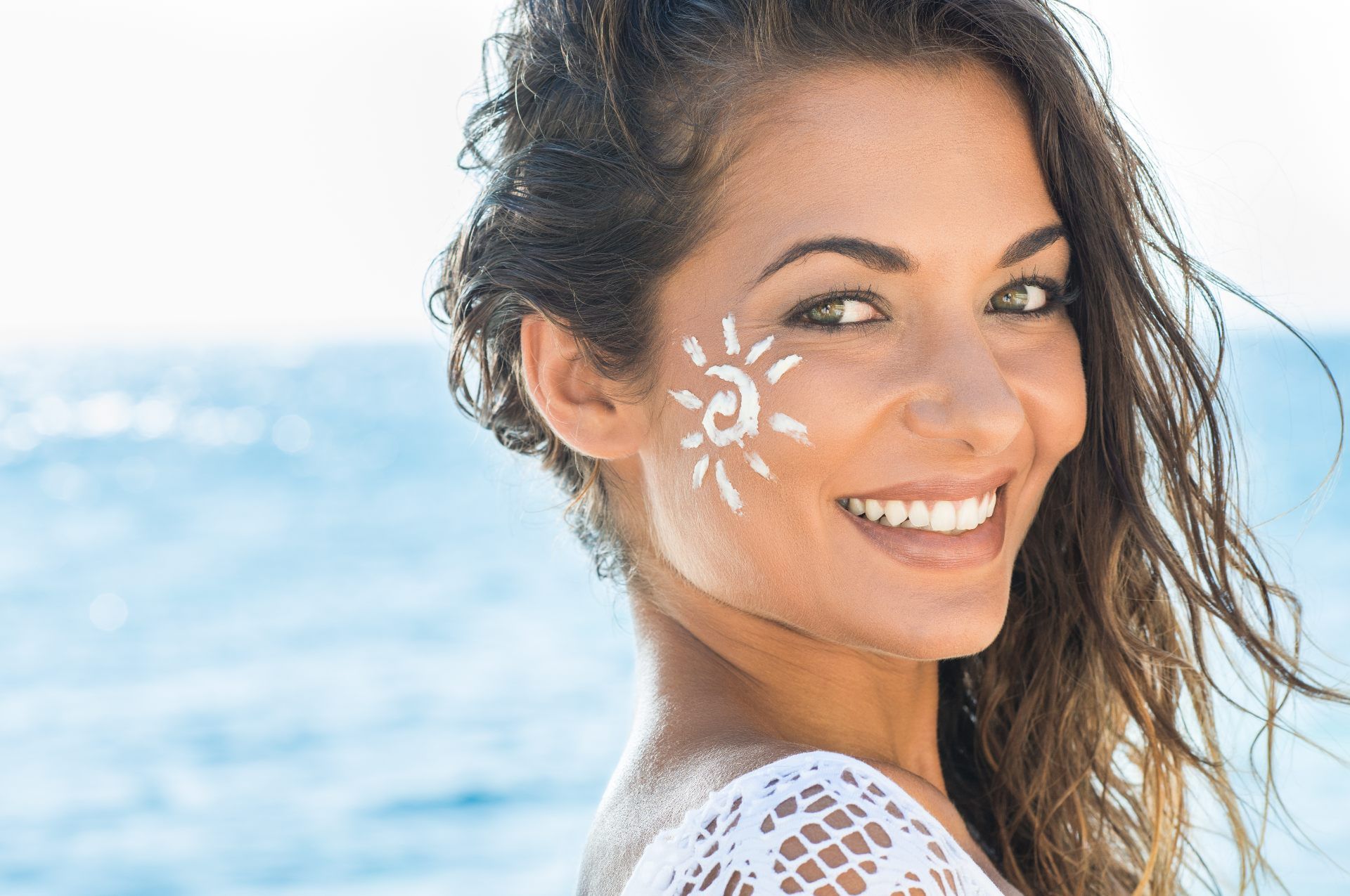 A smiling woman stands near water with sunscreen sun on her face - Coola sunscreen