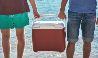 Two men carry a red cooler between them near the water - coleman ice cooler