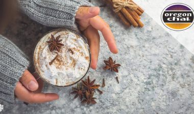 A person holds their hands around a chai latte in a cup, surrounded by spices - chai tea latte