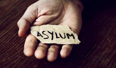 A person holds a torn piece of paper that reads "asylum" - remain in mexico policy