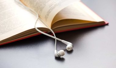 A set of white earbuds lie across an open book - Audible free trial