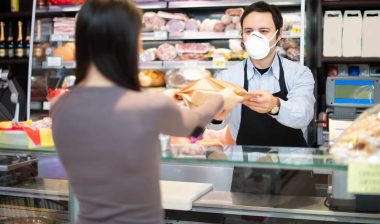 A deli counter worker wearing a surgical mask hands a woman her purchase - employee safety