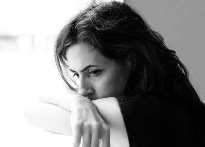 A dark-haired woman rests her chin on her arm, looking depressed or scared - sexual abuse