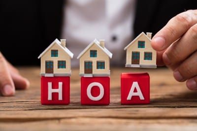 A man in a suit places tiny houses on top of red-and-white HOA letter blocks - black lives matter