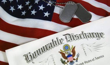 An honorable discharge certificate lies next to blank dog tags on top of a U.S. flag