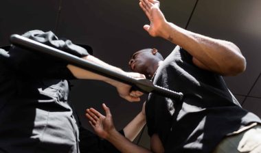 An officer uses a baton to stop a Black man with his hands in the air - police brutality