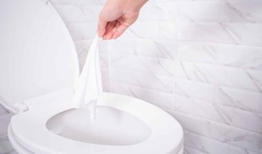 A person throws a wipe into a toilet near a white marble wall - flushable wipes
