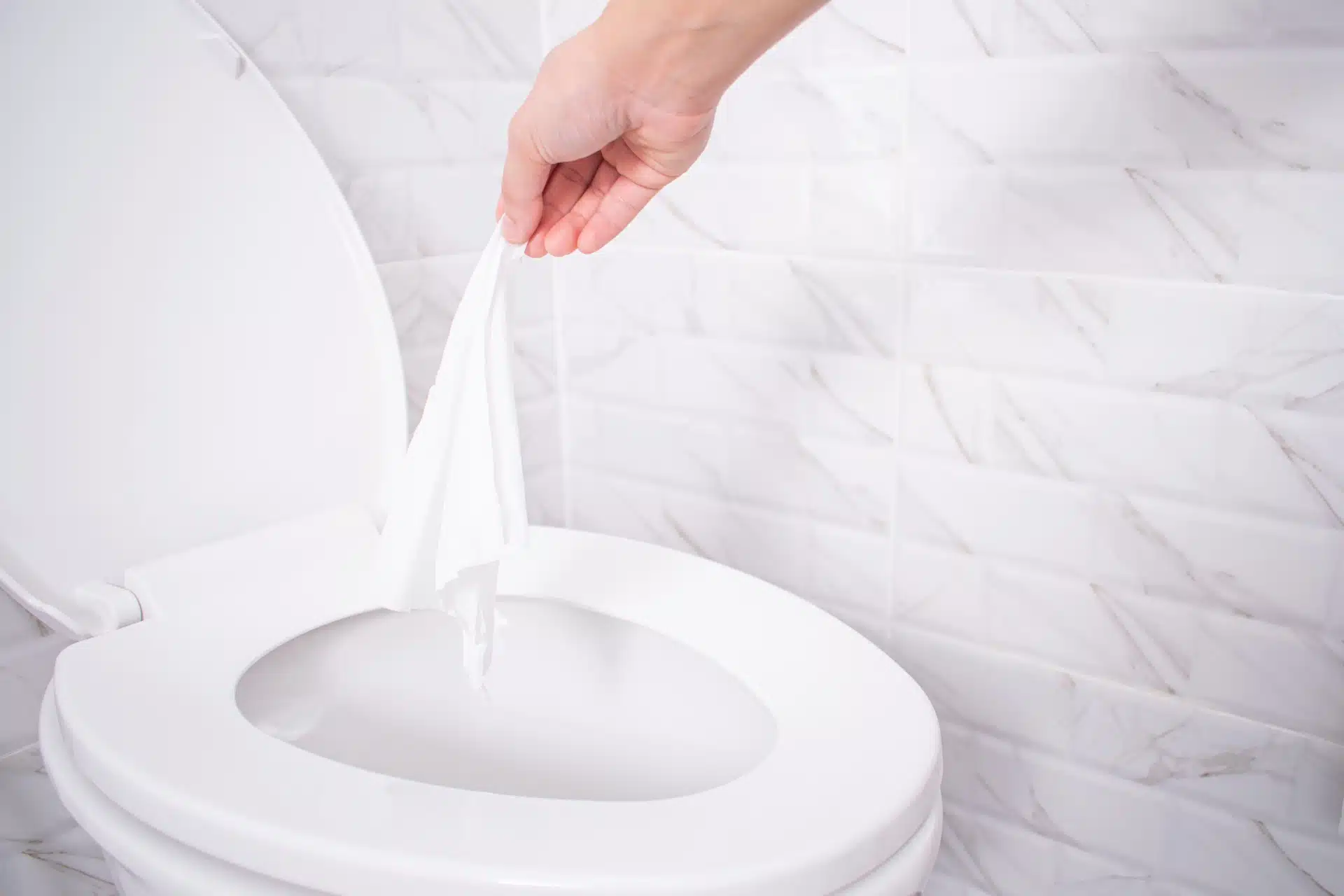 A person throws a wipe into a toilet near a white marble wall - flushable wipes