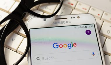 A Samsung smartphone with Google on the screen sits with glasses on top of a keyboard - Google tracking