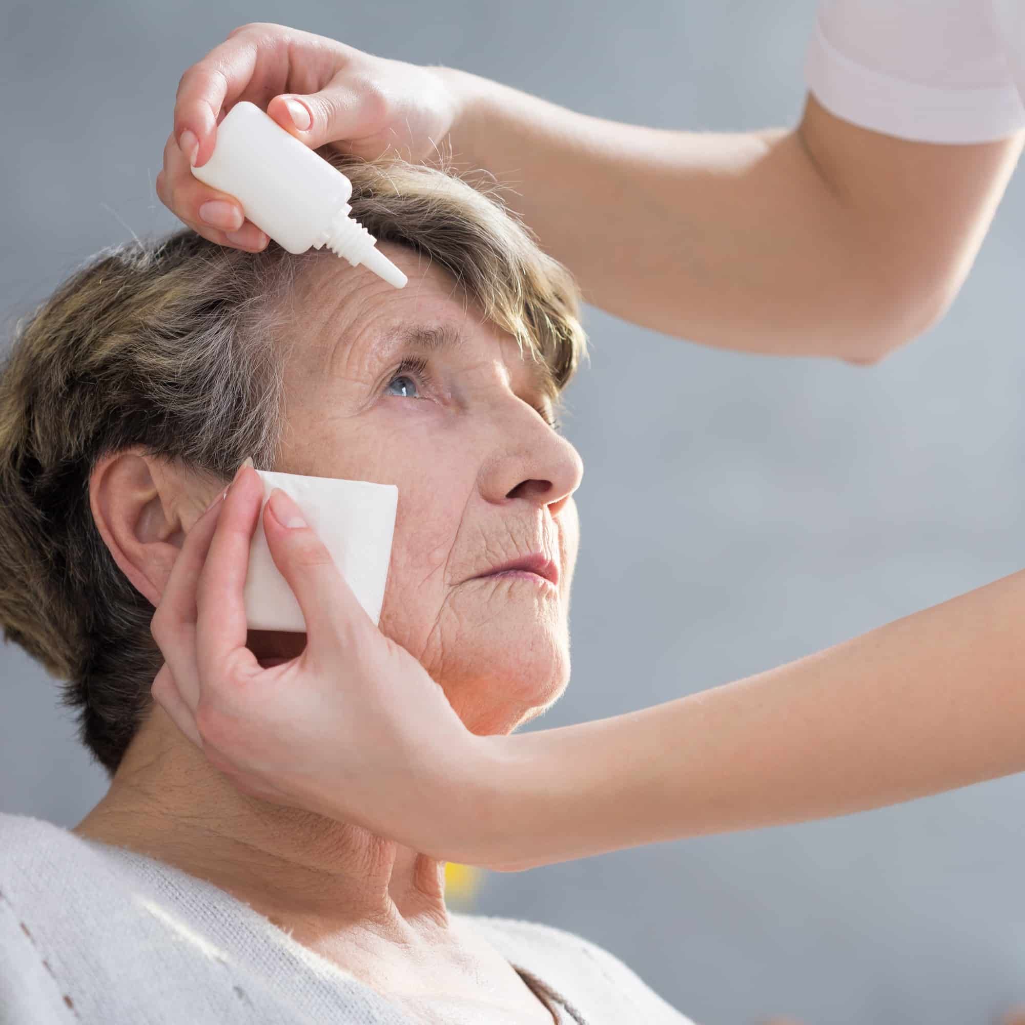 nurse administering eye drops to older female patient