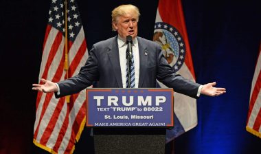 Donald Trump stands at a podium with his arms outstretched to his sides during a rally - Trump campaign