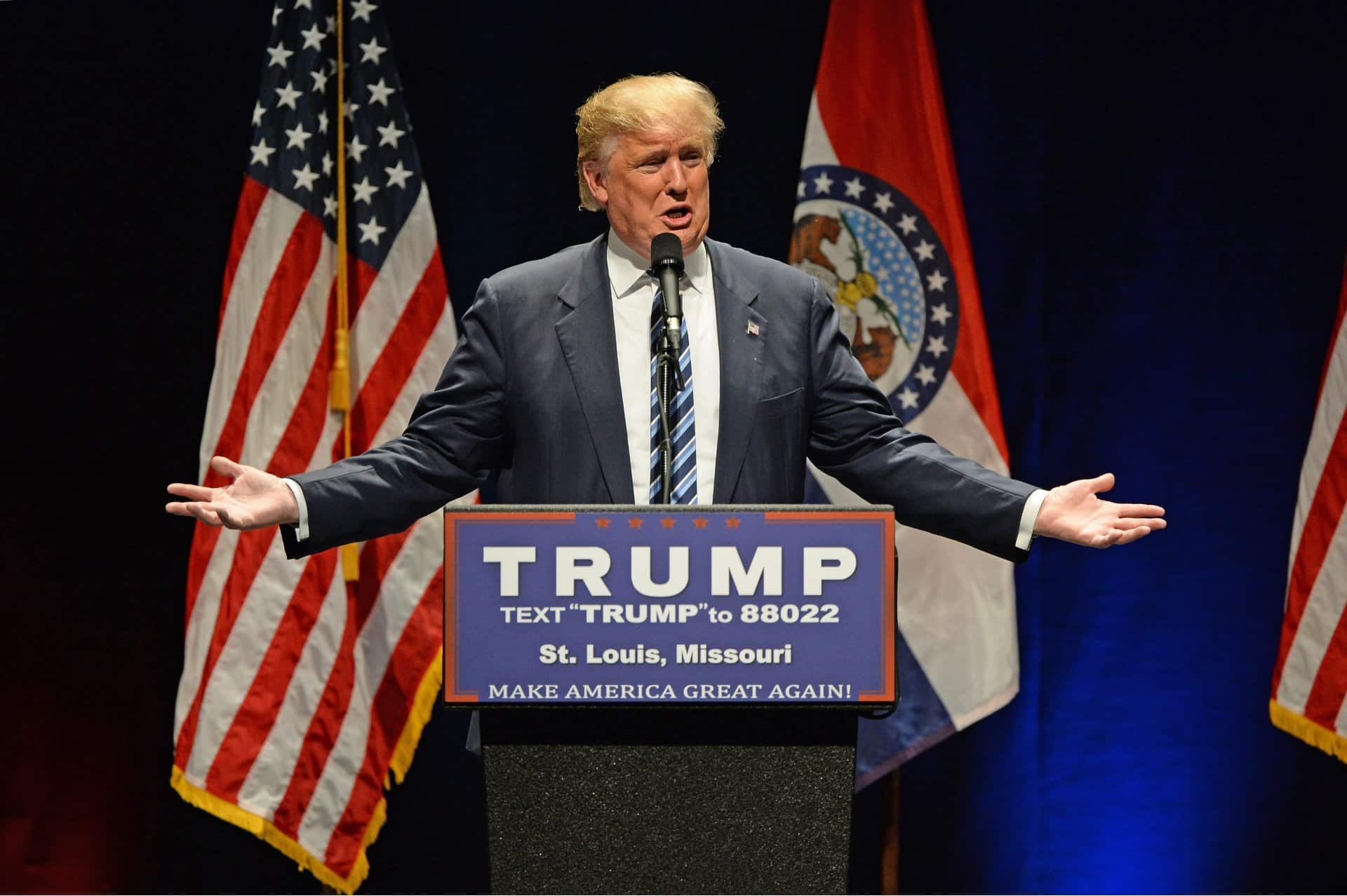 Donald Trump stands at a podium with his arms outstretched to his sides during a rally - Trump campaign