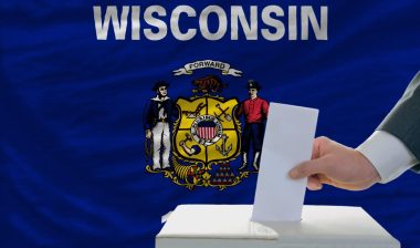 Man casts a ballot in front of a Wisconsin state flag - wisconsin voters