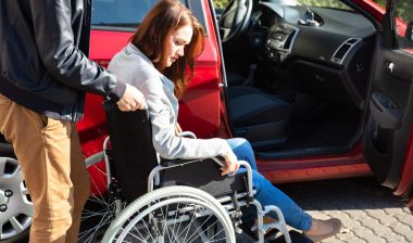 A man pushes a woman in a wheelchair up to the open passenger-side door of a red vehicle - Lyft wheelchair accessibility
