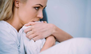 A blonde woman sits in bed, holding the blankets close to her face - sexual abuse