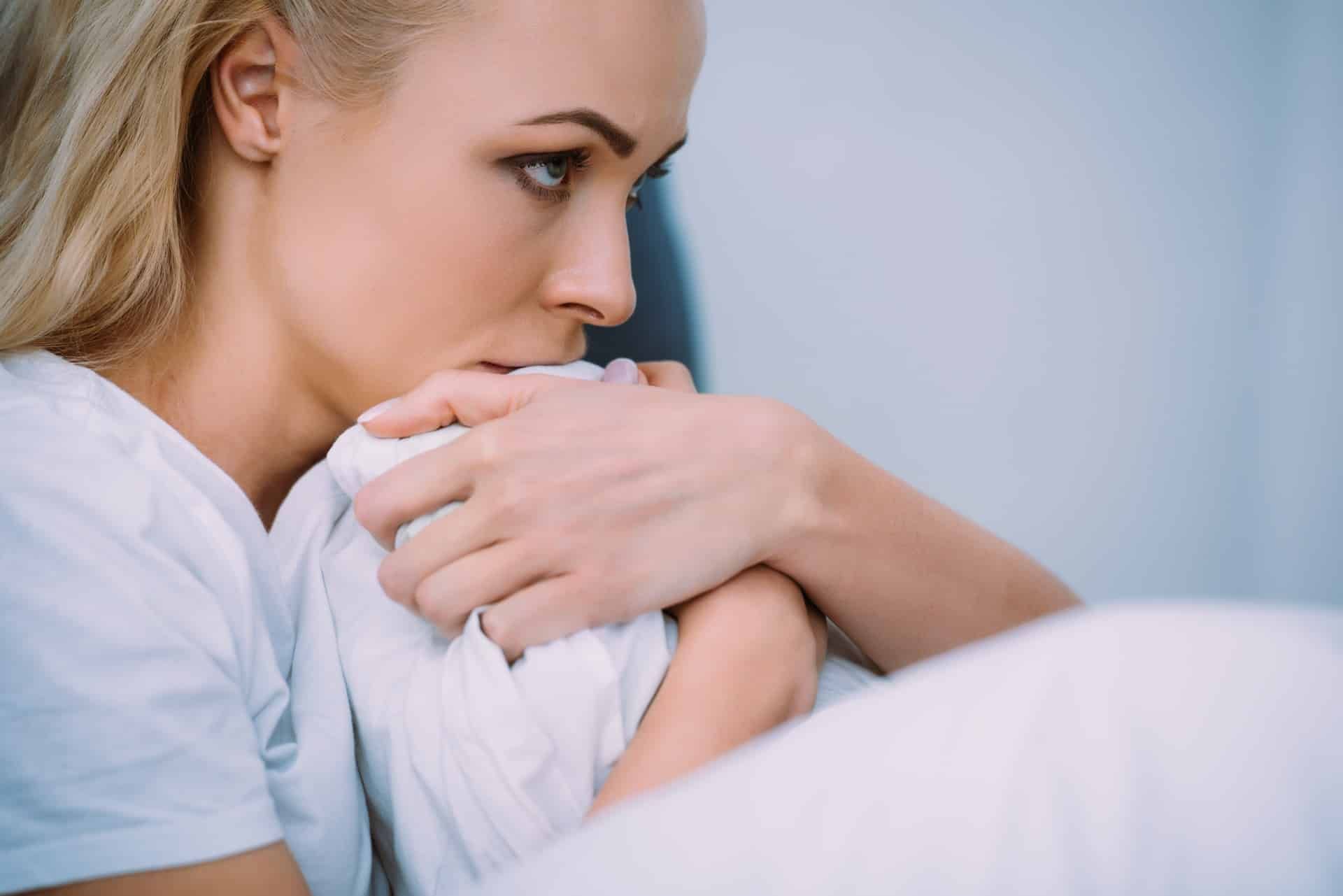 A blonde woman sits in bed, holding the blankets close to her face - sexual abuse