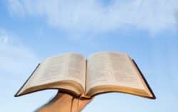 A man's hand holds an open Bible to the sky