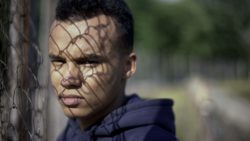 Serious teen boy stands next to chain link fence