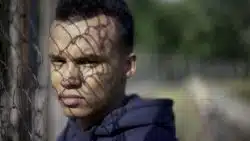 Serious teen boy stands next to chain link fence