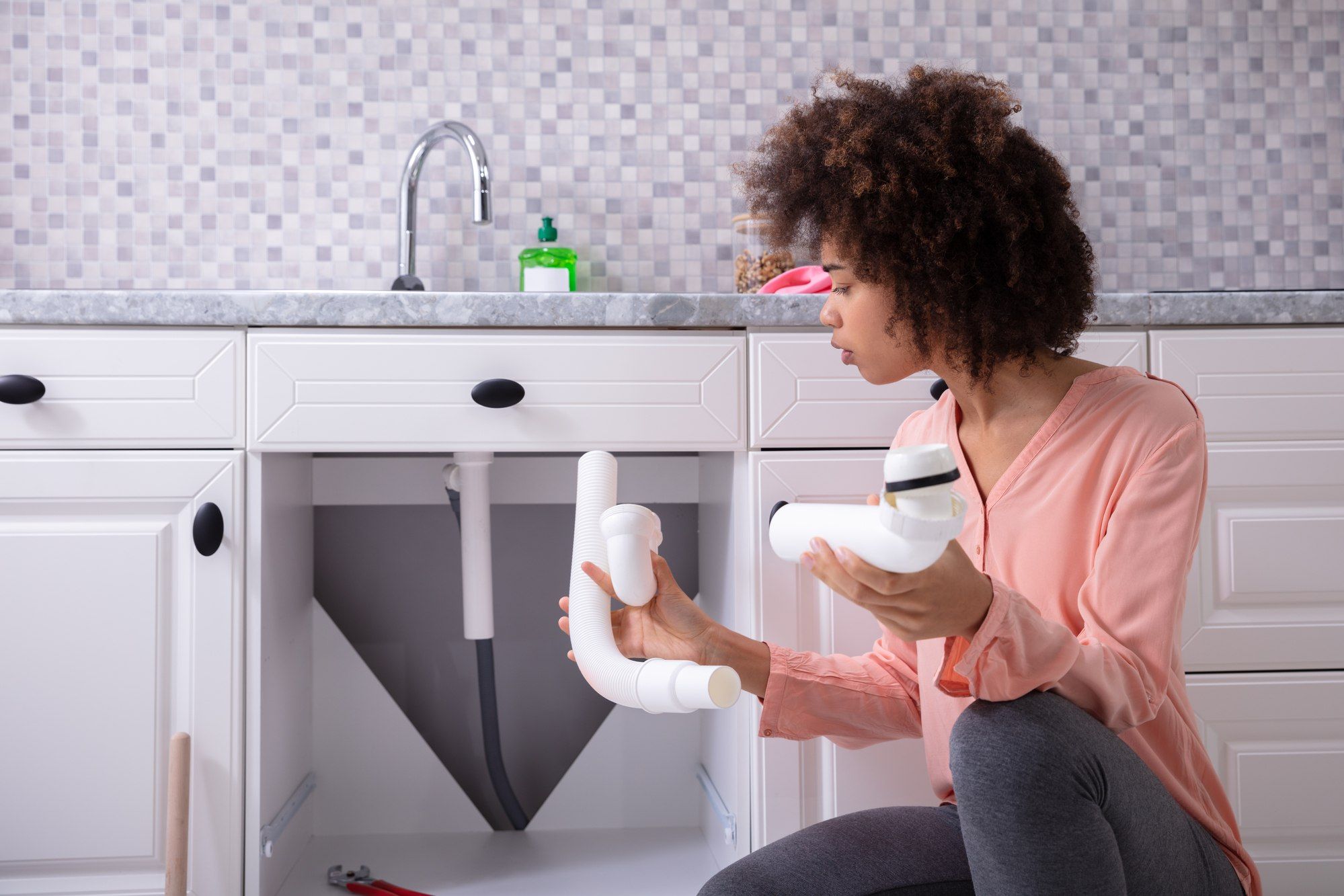 Woman inspects damaged pipes at kitchen sink