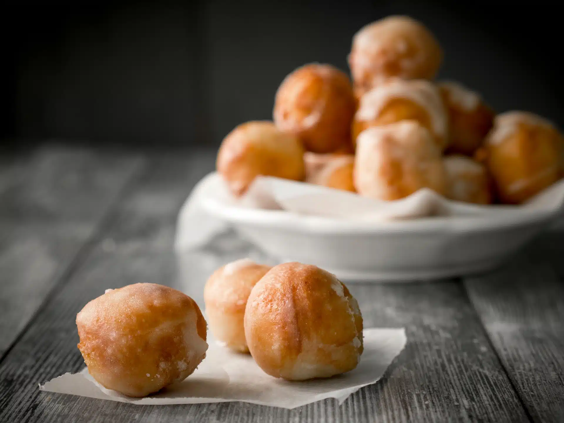 Three doughnut holes lie on a napkin in the foreground, with more stacked on a plate in the background - 7-Eleven donut holes