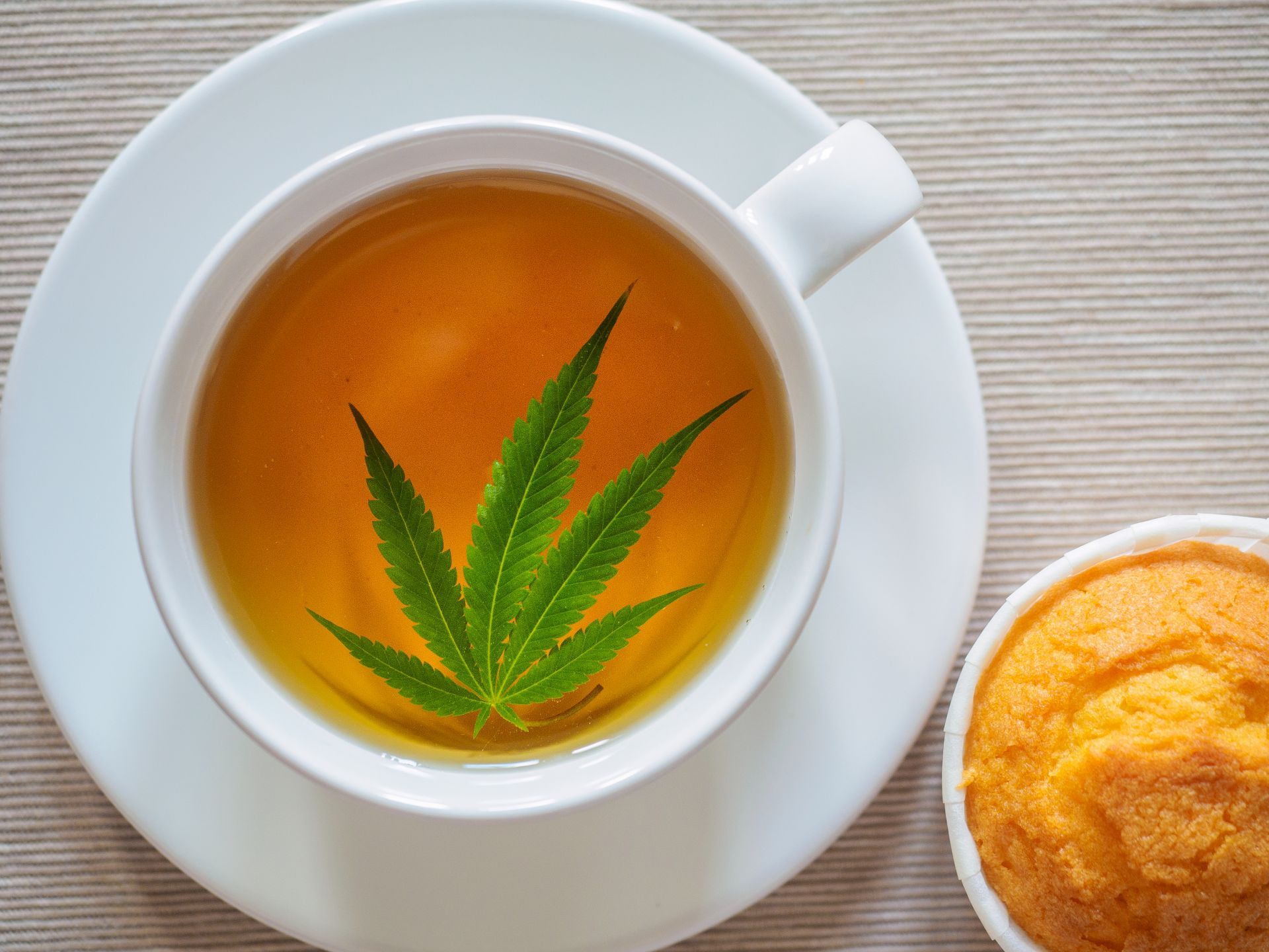 Hemp tea in a teacup with a hemp leaf, next to a muffin - Total Life Changes Tea