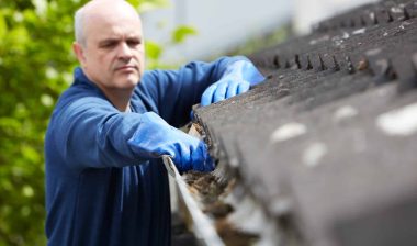 A man in blue gloves cleans the gutter on a house - LeafFilter gutter system