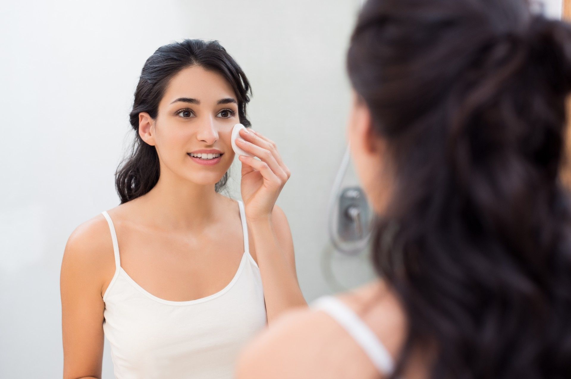A dark-haired woman smiles while cleaning her face - Murad Clarifying Oil-Free Water Gel